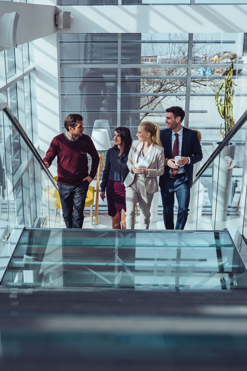 A group of diverse business professionals walking up a glass staircase in a modern office building, engaged